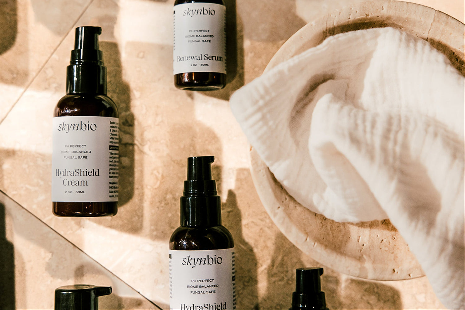Lifestyle image of Skynbio skincare products arranged in a soft pattern with a bowl and towel for launch page hero